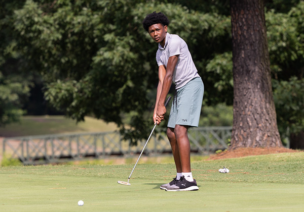 Young man in a grey polo lining up a putt on a golf green near a white flag.