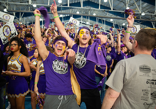 Cheerleaders from different NNPS highschools cheering on gym floor.