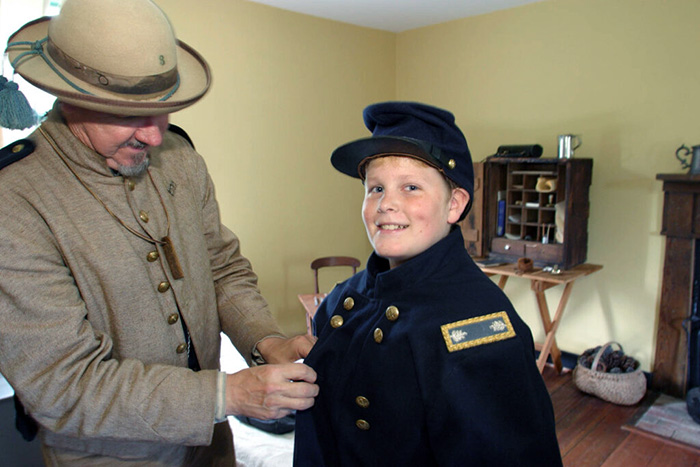 Adult helping a boy try on a Civil War Union soldier costume
