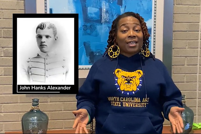 Woman in a North Carolina A&T sweatshirt presenting next to a historical photo of John Hanks Alexander